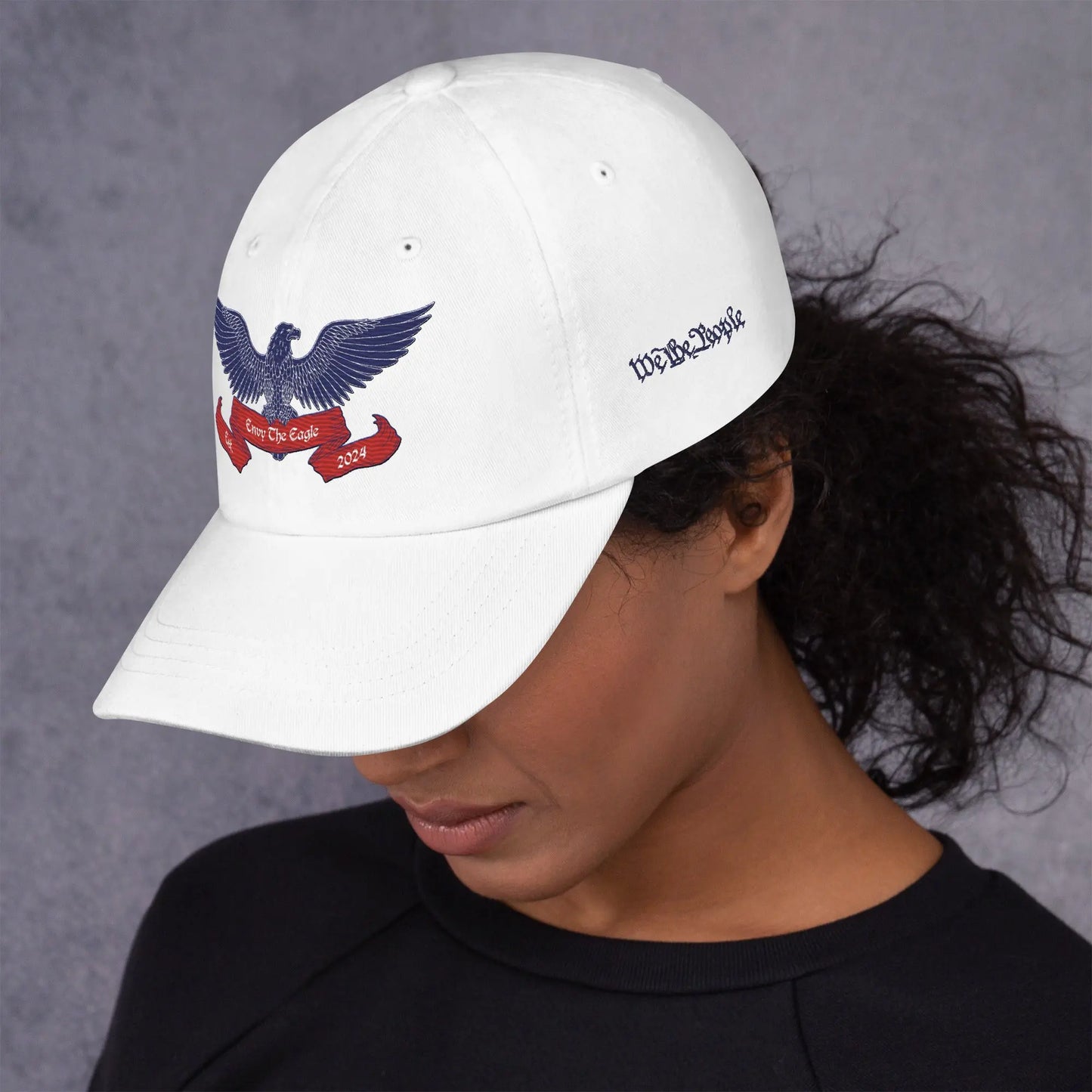 Woman wearing White embroidered baseball cap text We The People on left side Envy The Eagle™ Logo embroidered on front. Patriotism Love for Country